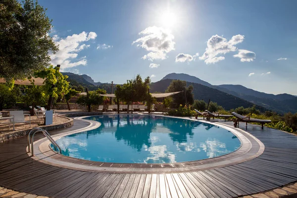 Swimming pool in the garden and beautiful sea and mountain landscape with trees and empty lounge chairs.