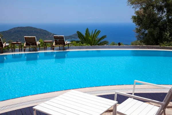 Swimming pool in the garden and beautiful mountain and sea landscape with trees and sunbeds.