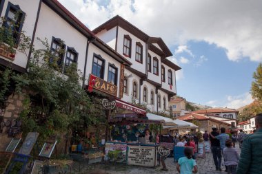 Ankara, Beypazari / Türkiye - 06.09.2020: Beypazari halkı güneşli bir günde sokakta yürüyor, eski bir sedir evi manzaralı.