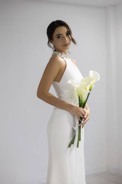 Kalla zambaklı şık beyaz gelinlikli romantik gelin, sakin ve güzel görünüyor.