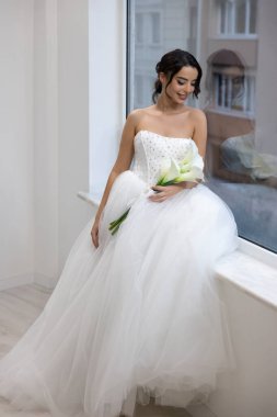 Kristal detaylı balo elbisesi içinde elinde çiçekler, zarif ve romantik bir portre olan mutlu gelin.