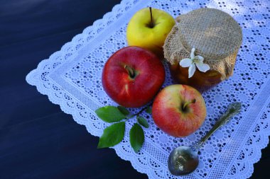Bir elma çiçeği, bir kaşık ve üç elma ile elma reçeli bir tencere, siyah ahşap bir masa üzerinde dantel bir bez üzerinde, üst görünümü