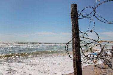 Ayağı ile plajda dikenli tel çit. Barbwire ve deniz görünümü