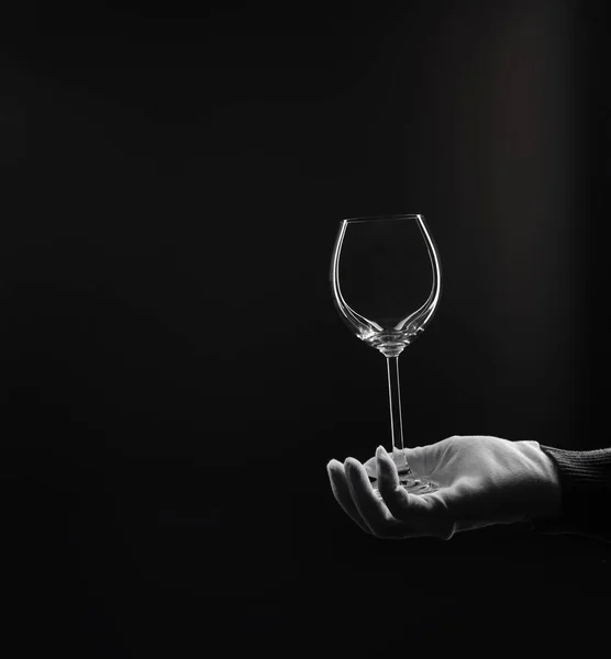 White glove with empty wine glass at isolated studio black background