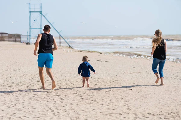 Father and kids run on the sea beach