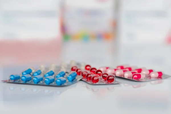 Medical pills in white, blue, red and other colors. Pills in plastic package on white mirror background. Concept of healthcare and medicine.