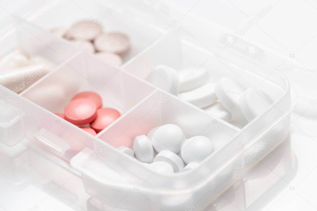 Close-up of pill case with various colorful pills, capsules on white background.