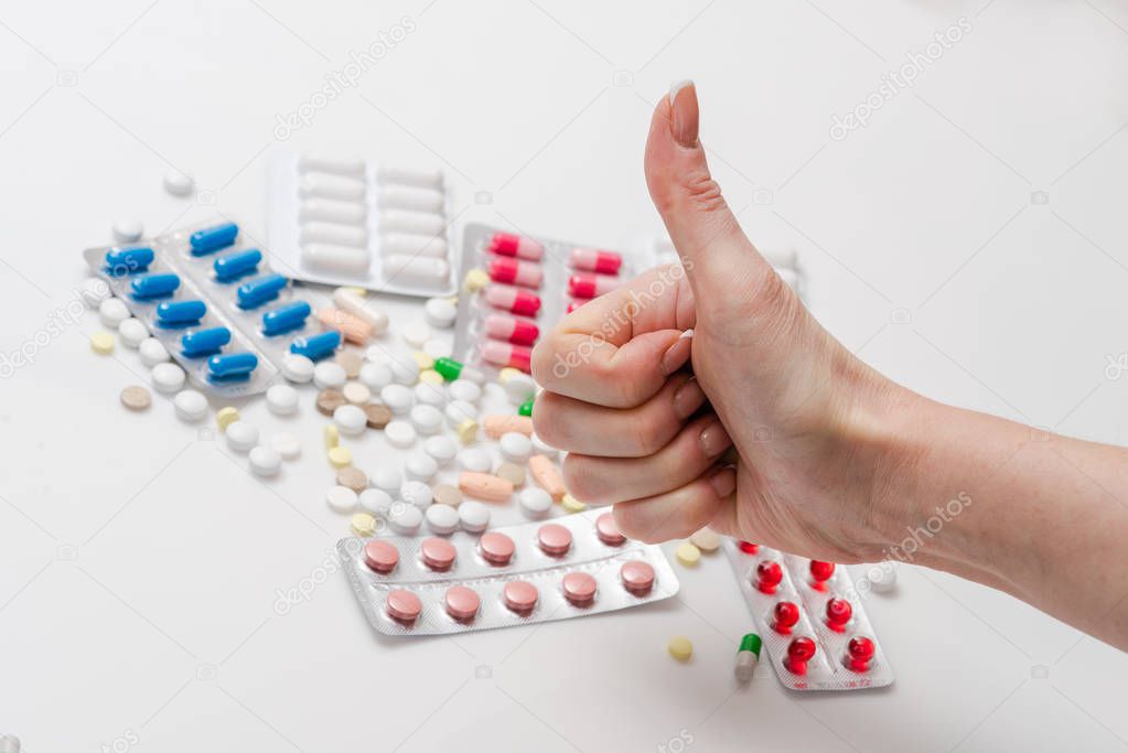 Female showing thumb up for medicine pills and tablets. Woman approve capsules and drugs at background put finger up. Top view.
