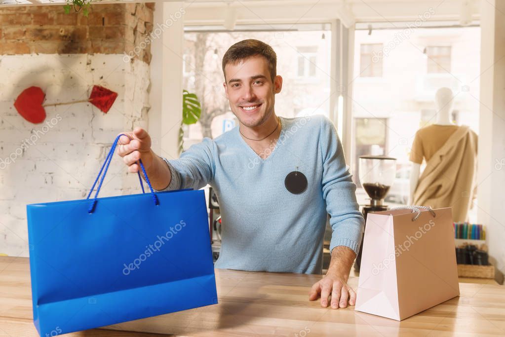 Smiling male give shopping bag in clothes store.