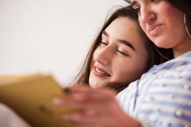 İki genç kadın yatakta kitap okuma