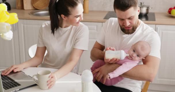 Mother with laptop and father feeds baby girl. — Stock Video