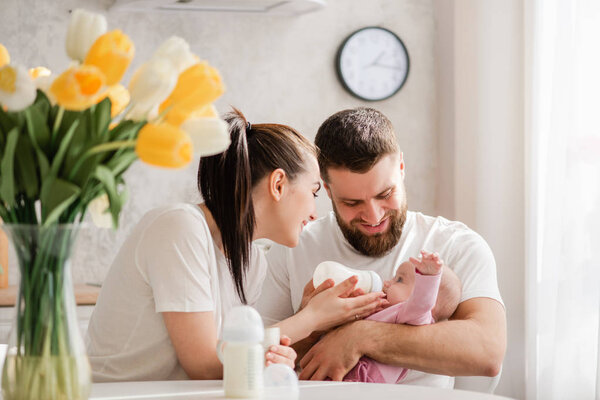 Счастливые молодые родители кормят младенца на кухне
