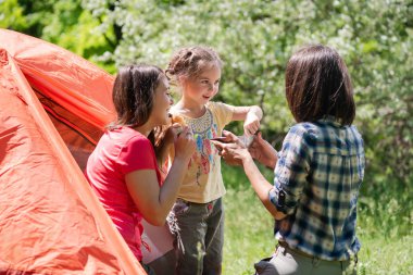 Metal plakalı çadırın yakınında iki kadın ve çocuk