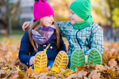 Sakız botu olan çocuklar sonbahar yapraklarında oturun