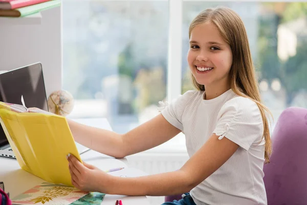 Sourire école preteen fille lecture livre à la table — Photo