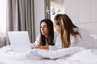 Yatakta dizüstü bilgisayarlı iki konsantre kadın.