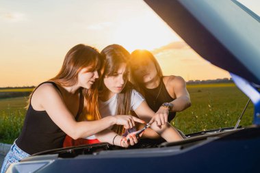Boş otoyolda takılıp kalmış, kaputu açık ve ingiliz anahtarıyla tamir edilmiş, seyahat sorunu olan bayan arkadaşlar.