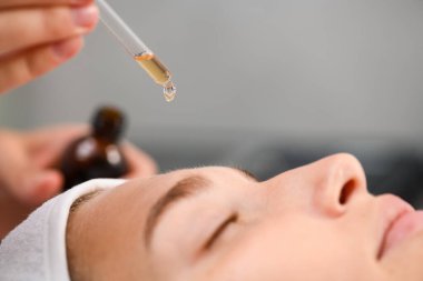 Güzellik salonunda yüz nemlendirici, yağ serumlu damlatıcı, kozmetolog müşterinin alnına ürün uygular.