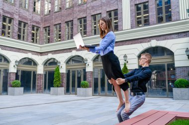 Genç adam ofis kıyafetleri içinde dizüstü bilgisayarı olan kadın bacakları tutuyor. İş merkezinde serbest çalışan insanlar için akroyoga konsepti.