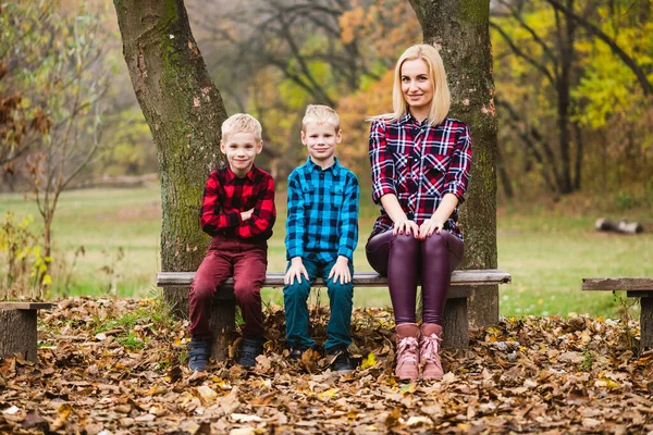 아름다운 어머니와 쌍동이 형제들은 공원의 벤치에 카메라 앞에서 미소를 짓는다 — 스톡 사진