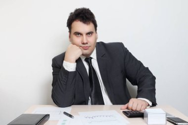 Takım elbiseli gülümseyen iş adamı defter, kağıt, kalem, hesap makinesi ile masada çenesini'den aksesuarlar