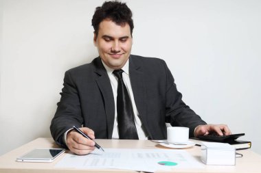 Takım elbiseli mutlu işadamı belgeleri masada kahve, diyagramları, belgeler, tablet Pc bakar