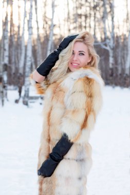 Genç ve güzel sarışın kürk ceket, deri eldiven açık kış gününde ormanda poz veriyor