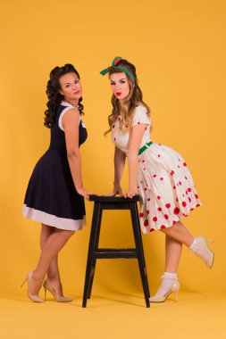 İki güzel kadın elbise poz dışkı, yakın sarı Studio pin biçemi, tam vücut