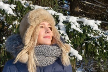 Genç ve güzel kadın kürk şapka güneş ışığı yeşil çam ağacı güneşli kış günü açık yakınındaki sahiptir