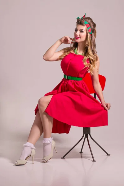 Smiling Girl Red Dress Hairdo Sits Chair Grey Studio Pin — Stock Photo, Image