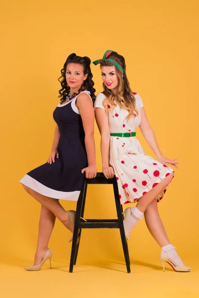 Dwie Młode Kobiety Pozie Sukienki Żółty Studio Pobliżu Stołek Upiąć — Zdjęcie stockowe