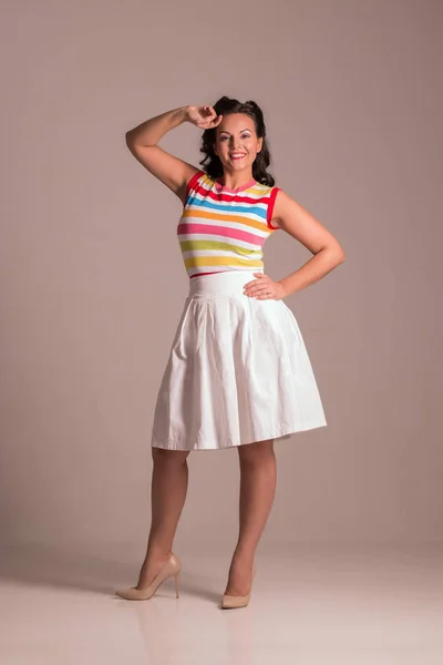 Beautiful woman in skirt with hairdo poses in grey studio, pin up style, full body