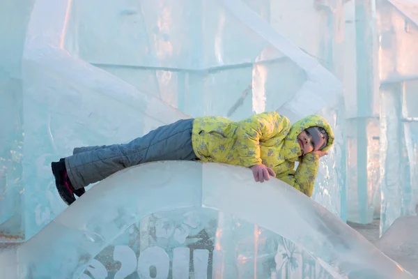 穿着黄色保暖衣服的快乐女孩在冬天的冰雕上躺着 — 图库照片