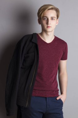 Yakışıklı çocuk genç tişört, ceket ile duvara yakın gri studio duruyor.