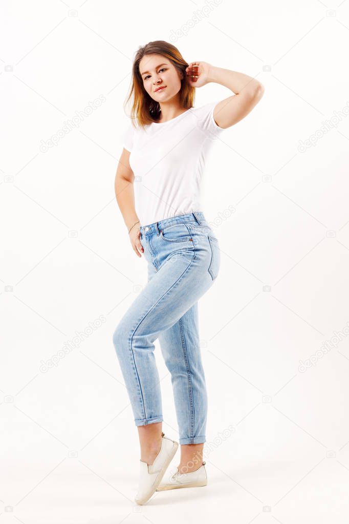 Beautiful girl teenager in white t-shirt and jeans poses in white studio, full body