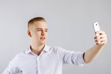 Genç mutlu sarışın adam beyaz gömlekli smartphone ile selfie studio yapar.