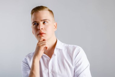 Beyaz tişörtlü genç yakışıklı adam çenesine dokunuyor ve stüdyoda düşünüyor