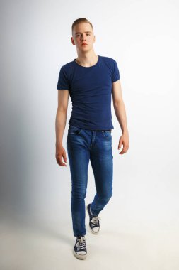 Genç yakışıklı erkek mavi tişört ve kot pantolon, beyaz studio, tam vücut gider