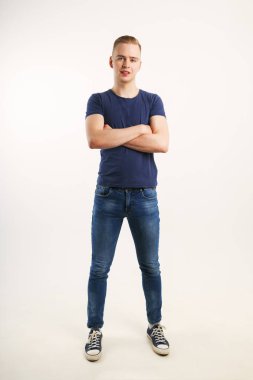 Yakışıklı delikanlı mavi tişört ve kot pantolon beyaz Studio, tam vücut çapraz silah ile poz veriyor