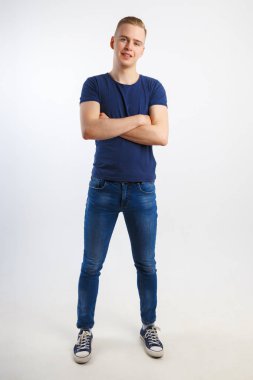 Mutlu yakışıklı delikanlı mavi tişört ve kot pantolon beyaz Studio, tam vücut çapraz silah ile poz veriyor
