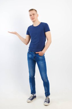 Mutlu yakışıklı delikanlı mavi tişört ve kot pantolon bir şey beyaz studio, tam vücut gösterir