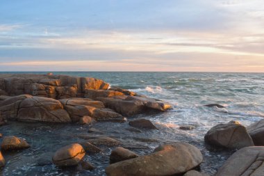 Sahilde batan güneş sırasında rüzgar serin eser. Kumlu zeminile güzel bulutlar ve kayalar