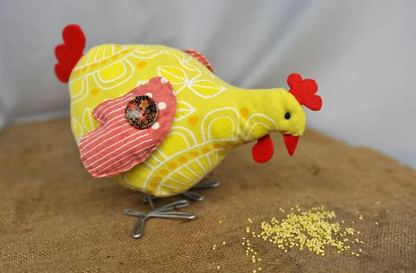 Closeup of handmade toy chicken on burlap background eating millet