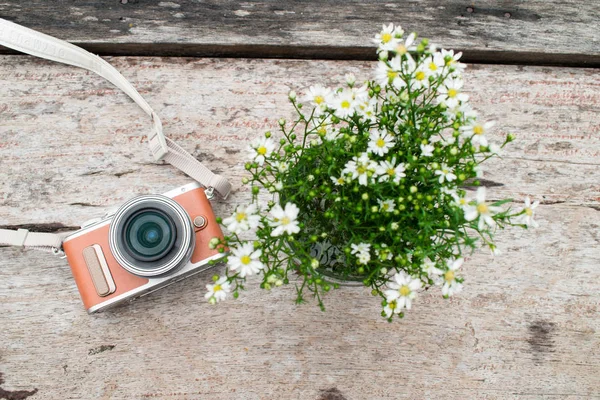 Camera with white flower vase on old brown wooden desk. Top view.