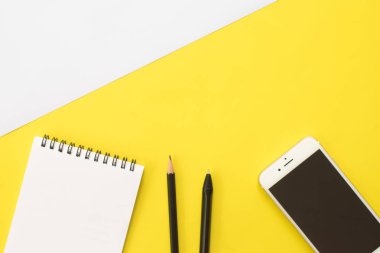 Sarı arka planda kitap, kalem, kalem, akıllı telefon ve gözlük. Yaşam tarzı çalışma alanı, Üst görünüm.