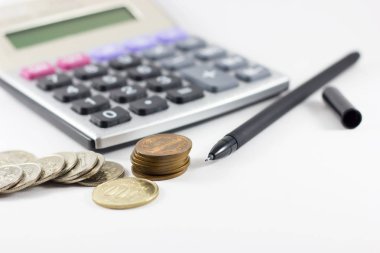 Beyaz arka plan üzerinde hesap makinesi, bozuk para ve kalem.