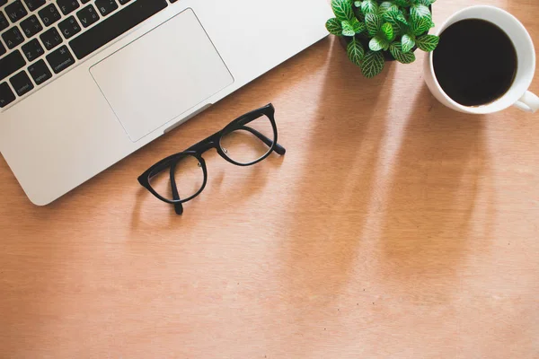 Coffee, computer, eyeglasses  and tree pot on brown wooden desk in office, Workspace.