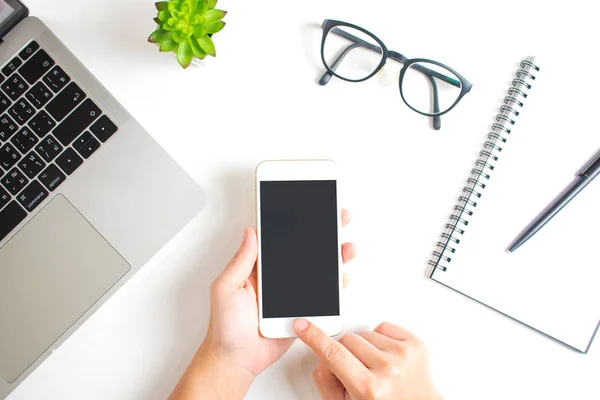 Manos usando un teléfono inteligente en una mesa blanca moderna con computadoras portátiles a — Foto de Stock