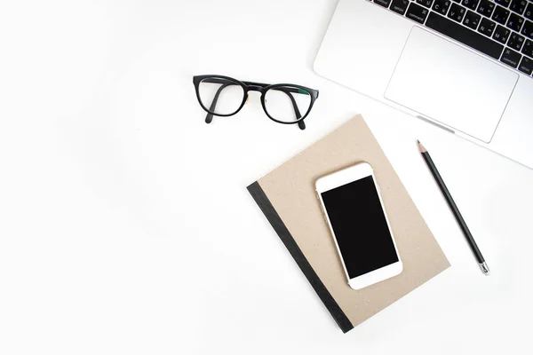 Bílá kancelářská deska s notebookem, inteligentními telefony, sklenicemi a notesem — Stock fotografie