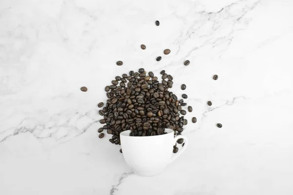 Перевернутый белый стакан и кофейные зёрна на мраморном похлопывании — стоковое фото